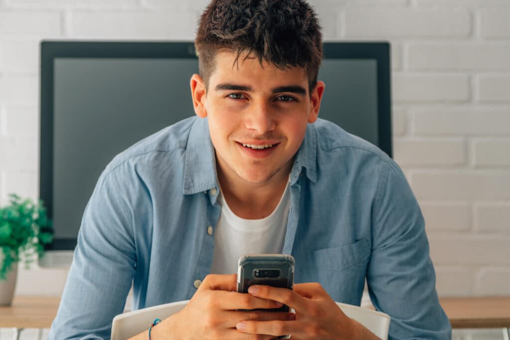 portrait of young teenager with mobile phone in hands and computer in the background